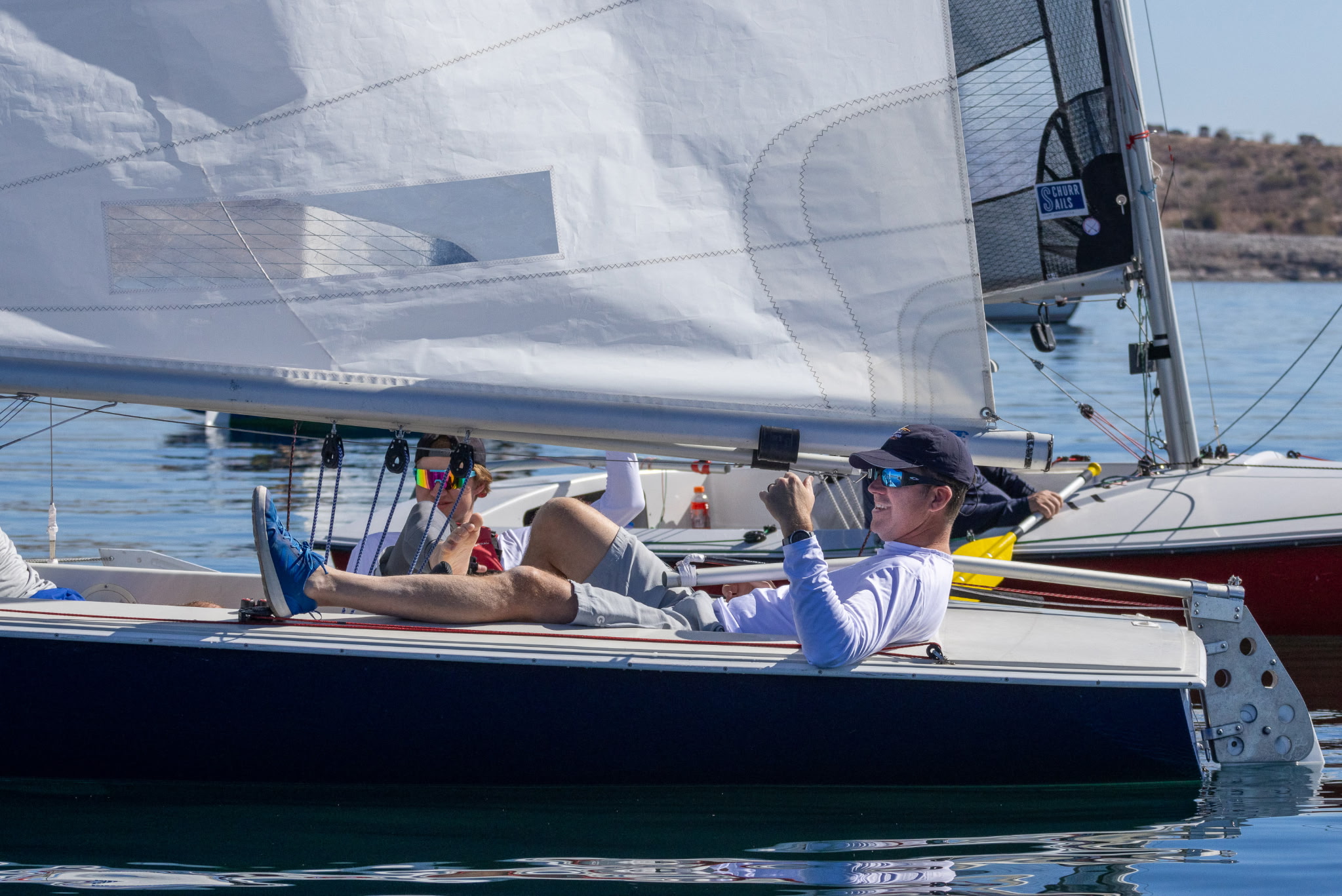 small blue becalmed sailboat with man relaxing with his foot up
