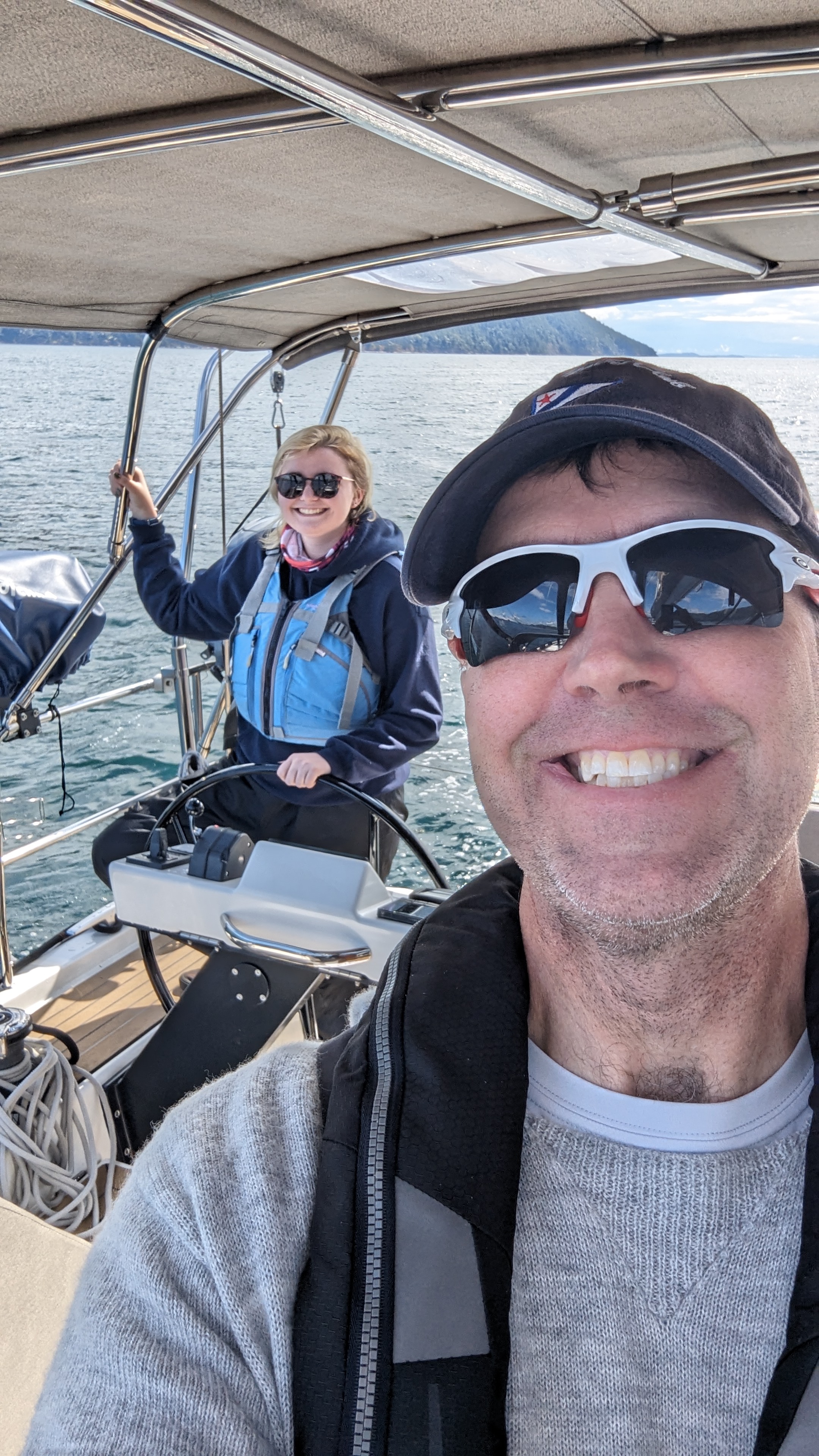 Man taking selfie with teen daughter at the helm of a sailboat